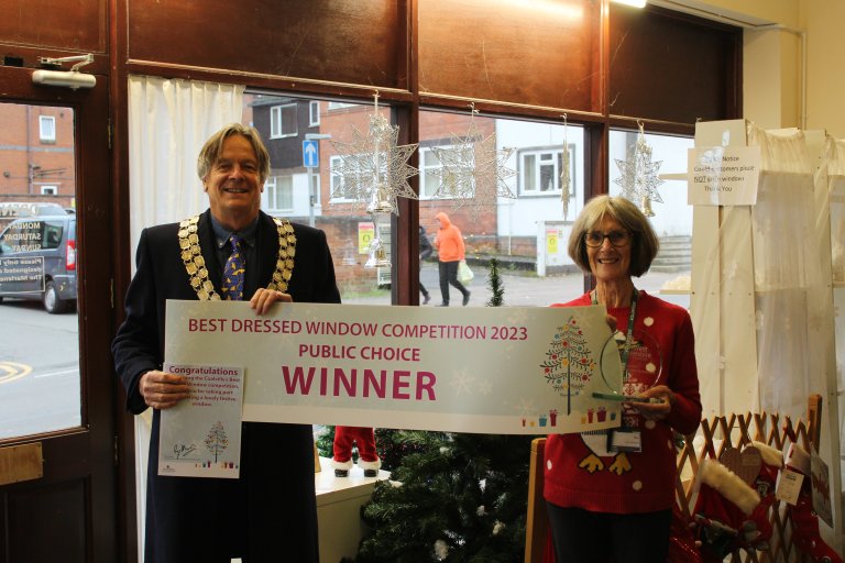 Picture of a man (Chairman Cllr Ray Morris) and a woman (shop owner of The Attic), holding a banner declaring the shop as the winner of the public vote for the 2023 Best Dressed Window Award in Coalville.