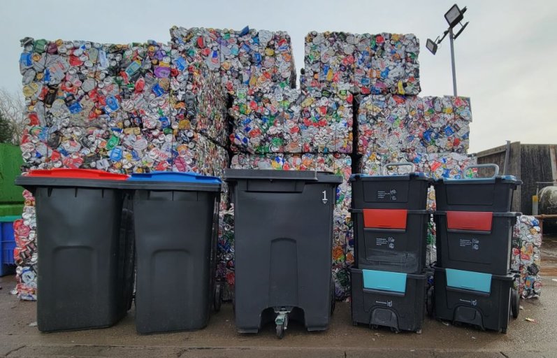 Three different types of recycling bins in front of large stacks of aluminium bales