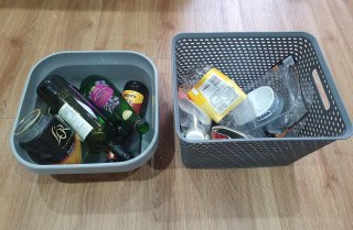 A washing up bowl containing glass recycling and a separate plastic basket containing plastic and metal recycling
